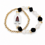 A set of two beaded stretch bracelets on a white background. One bracelet features gold-toned beads, white faux pearls, and black faceted beads, with a white rectangular charm displaying a red and black joker card graphic and the word 'JOKER'.