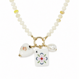 A beaded necklace with light yellow, white beads, featuring gold-tone hardware and three charms: a white heart with colorful floral, a white pearl bead, and a white rectangular tile charm printed with pink and green flower number 4 resembling mahjong tiles.