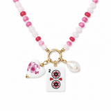 A beaded necklace with pink and white beads, a gold clasp, and three charms: a white heart with a pink floral design, a white rectangular tile charm with a red and black symbol, and a white pearl bead.