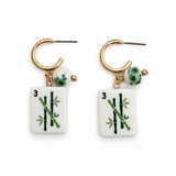 A pair of gold hoop earrings with dangling white rectangular tiles printed like mahjong tiles, featuring green bamboo motifs and small green bead accents, shown on a plain white background.