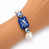 Bracelet with blue square bead featuring a white design and pearl beads on a wrist.