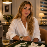 Woman sitting at a table with a glass of whiskey and playing dominoes in a cozy room.