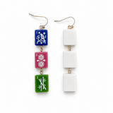A pair of dangling earrings on a white background. One earring has three rectangular tiles in blue, pink, and green with white Japanese-style symbols, and the other has three plain white rectangular tiles.