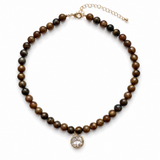 A beaded necklace featuring alternating brown and black tiger's eye beads, finished with a gold-tone extender chain and a round clear crystal pendant on a white background.