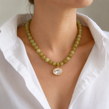 Necklace with green beads and a gold pendant worn by a person in a white shirt.