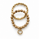 gold bead and light brown taupe color beaded bracelet with a con crysal charm on white bavkground