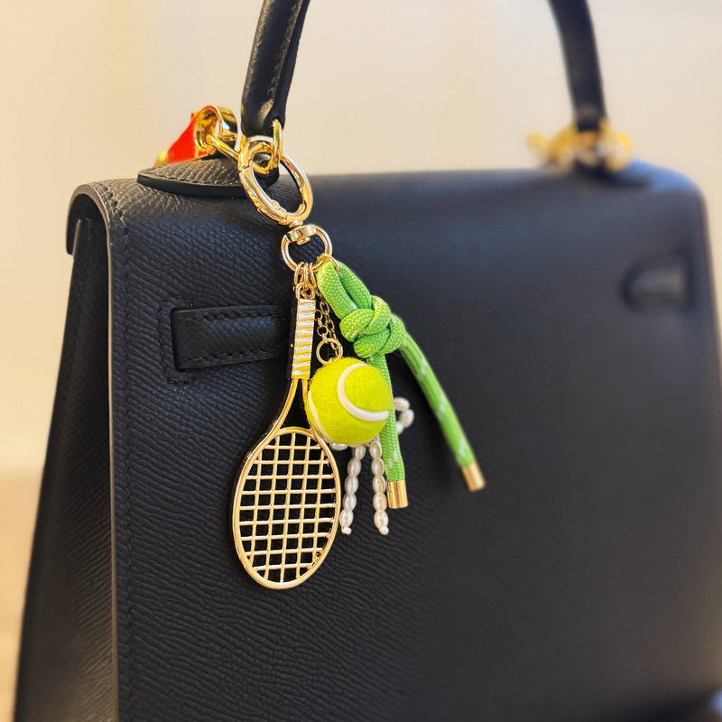 Gold-tone tennis-themed bag charm featuring a miniature racket, neon green tennis ball, and light green ribbon accents