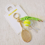 Gold-tone tennis-themed bag charm featuring a miniature racket, neon green tennis ball, and light green ribbon accents