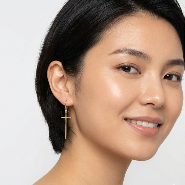A pair of gold-tone molten-style cross earrings featuring a sleek, abstract design with a softly curved silhouette and minimal detailing, hanging vertically from simple hooks. on model