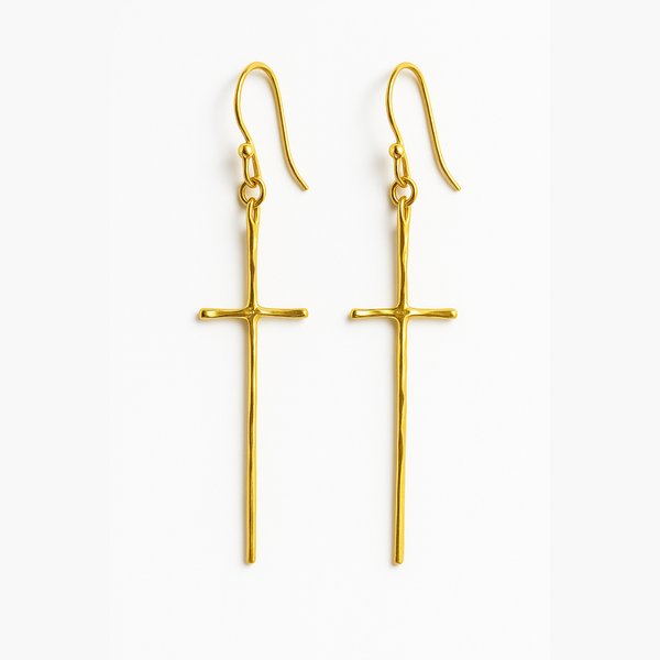 A pair of gold-tone molten-style cross earrings featuring a sleek, abstract design with a softly curved silhouette and minimal detailing, hanging vertically from simple hooks.
