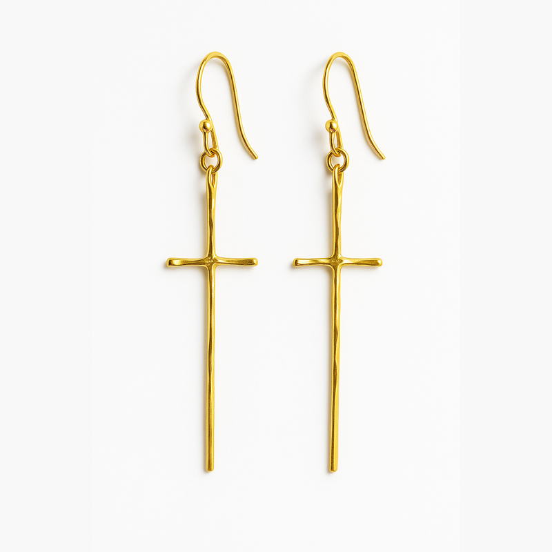 A pair of gold-tone molten-style cross earrings featuring a sleek, abstract design with a softly curved silhouette and minimal detailing, hanging vertically from simple hooks.