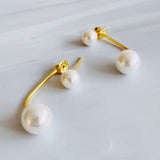 A pair of modern pearl earrings featuring a sleek gold-tone bar connecting two lustrous pearls—one smaller and one larger—for a minimalist yet elegant look. These dual pearl drop earrings combine classic sophistication with a modern silhouette.
