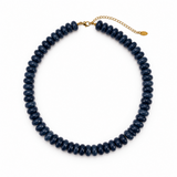 A dark navy blue beaded necklace with a gold clasp and extender chain, displayed on a clean white background.