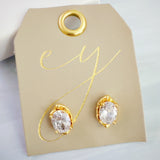 Chic stud earrings featuring a fluid, molten metal frame wrapped around a sparkling oval-cut crystal, offering a refined mix of organic shape and radiant shine.