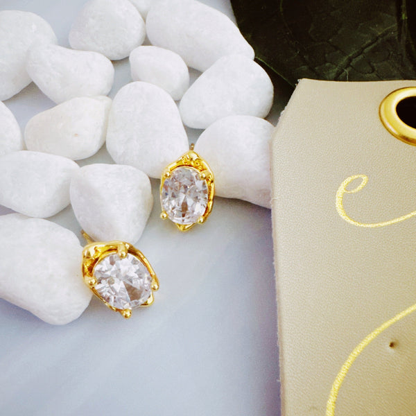 Chic stud earrings featuring a fluid, molten metal frame wrapped around a sparkling oval-cut crystal, offering a refined mix of organic shape and radiant shine.