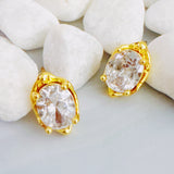Chic stud earrings featuring a fluid, molten metal frame wrapped around a sparkling oval-cut crystal, offering a refined mix of organic shape and radiant shine.
