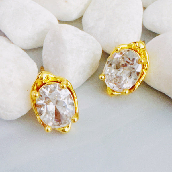 Chic stud earrings featuring a fluid, molten metal frame wrapped around a sparkling oval-cut crystal, offering a refined mix of organic shape and radiant shine.