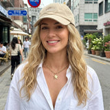 Woman wearing a beige cap and white shirt with a star necklace on a city street.