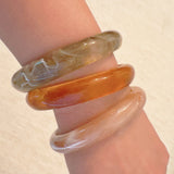 Set of three bold resin bangles in natural earth tones, featuring a mix of marbled and solid finishes for a stylish stacked look.