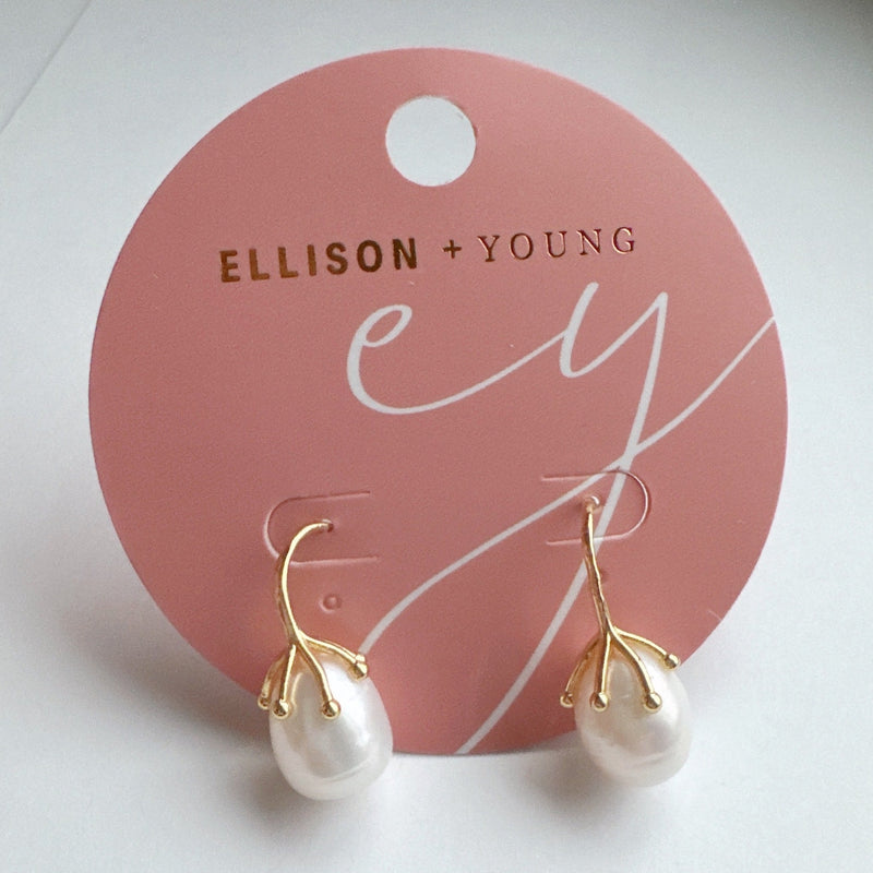 A pair of elegant drop earrings featuring organic-shaped baroque pearls with gold-tone vine-like prong detailing, suspended from sleek curved gold hooks, displayed against a dark textured background.