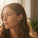 A pair of elegant drop earrings featuring organic-shaped baroque pearls with gold-tone vine-like prong detailing, suspended from sleek curved gold hooks, displayed against a dark textured background.