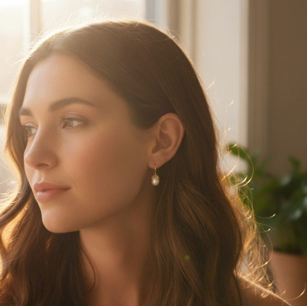 A pair of elegant drop earrings featuring organic-shaped baroque pearls with gold-tone vine-like prong detailing, suspended from sleek curved gold hooks, displayed against a dark textured background.