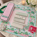 Ellison+Young Palm Resort Mahjong Complete Set styled in a tropical, resort-inspired lifestyle scene with the tile set, storage bag, and playing mat.
