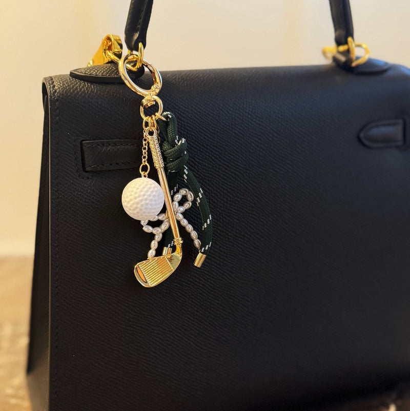 Gold-tone golf-themed bag charm featuring a miniature golf club, white golf ball, and forest green ribbon accents