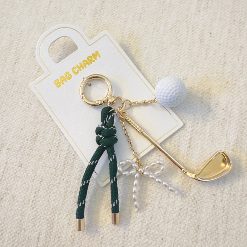 Gold-tone golf-themed bag charm featuring a miniature golf club, white golf ball, and forest green ribbon accents
