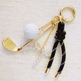 Gold-tone golf-themed bag charm featuring a miniature golf club, white golf ball, and forest green ribbon accents