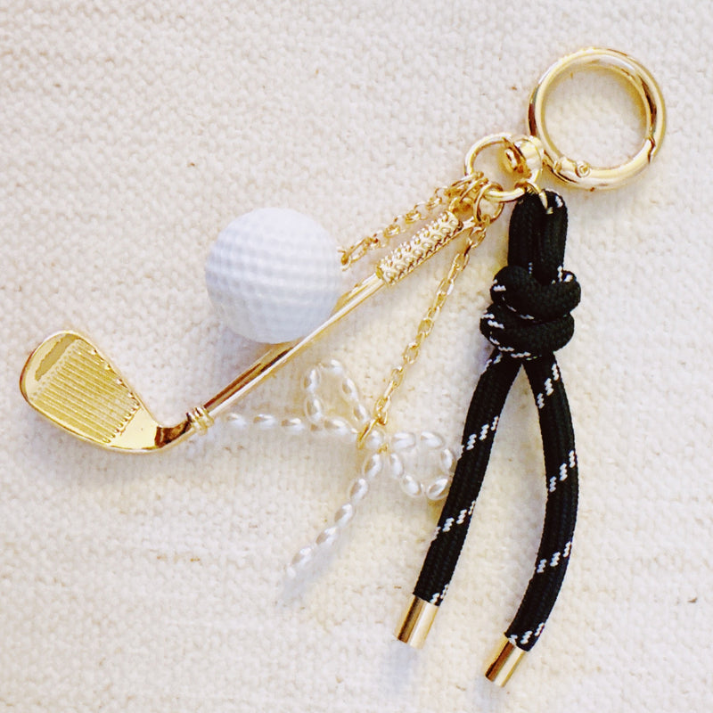 Gold-tone golf-themed bag charm featuring a miniature golf club, white golf ball, and forest green ribbon accents