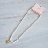 Refined pearl necklace featuring a small gold heart pendant adorned with sparkling crystals. The minimalist yet elegant design offers a timeless touch perfect for layering or wearing on its own.