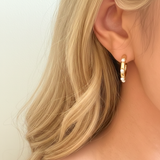Polished gold hoop earrings adorned with small white pearls evenly spaced around the hoop. The design combines modern structure with classic pearl accents for a refined yet trendy look.
