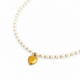 Necklace with gold heart charm and white beads on a white background