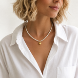 Woman wearing a pearl necklace with a gold heart pendant, dressed in a white shirt.