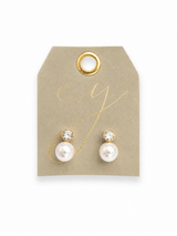 Gold stud earrings featuring round clear crystal accents paired with glossy white pearl drop details in a classic and elegant design on leather card