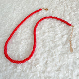Close-up of a bold red beaded necklace featuring uniformly round, glossy beads strung together in a classic strand, creating a vibrant and timeless accessory.
