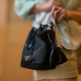 Black handbag with a bow held by a person against a blurred background