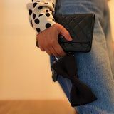Person holding a black quilted handbag with a bow detail.