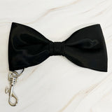 Black bow tie with a metal clasp on a light wooden surface