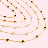 Gold necklaces with colorful clover-shaped pendants on a light pink background