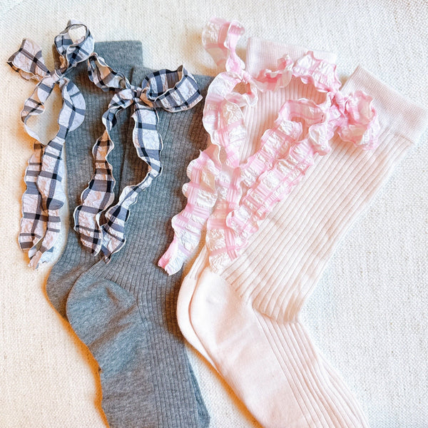 Set of two socks featuring plaid patterns with ruffle bow accents, combining classic charm with playful, feminine details.