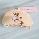 Preppy-inspired bear hair claw clips featuring fashionable teddy bear dressed in vintage collegiate outfits. Each clip showcases a different bear character on a pastel background, adding a playful yet polished touch to any hairstyle.