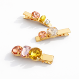 Two gold hair clips with colorful gemstones on a white background