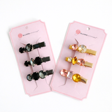Two packages of hair clips with colorful rhinestone designs on a white background.