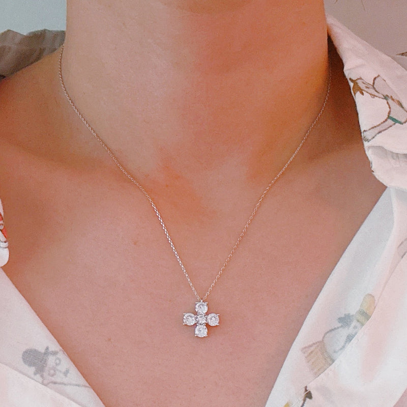 Silver cross pendant necklace featuring a symmetrical arrangement of radiant-cut cubic zirconia stones, creating a brilliant and elegant sparkle on a fine silver chain.