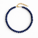 A collection of polished gemstone bead necklaces in various colors, including deep blue, green, brown, pink, and cream. Each necklace features smooth, rounded beads with a glossy finish, offering a timeless and versatile accessory look.