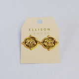 Close-up of a pair of round gold-tone stud earrings featuring a raised elephant motif on a medallion-style base with detailed edge accents.