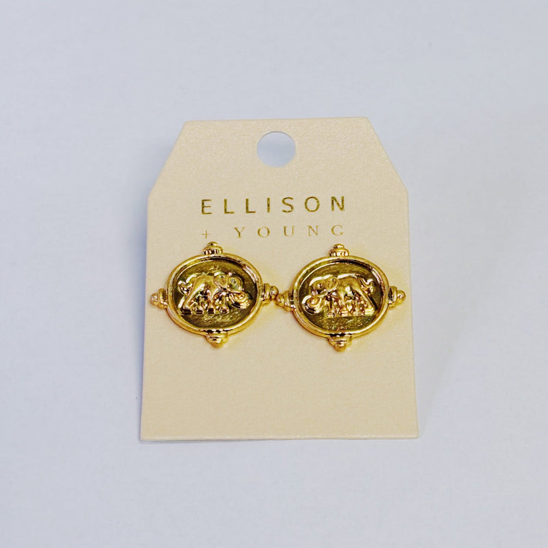 Close-up of a pair of round gold-tone stud earrings featuring a raised elephant motif on a medallion-style base with detailed edge accents.