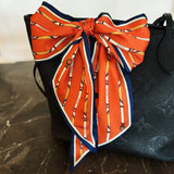 Orange patterned scarf tied around a black handbag on a marble surface